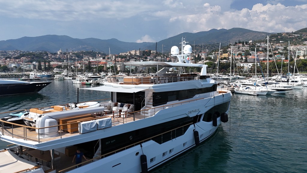A luxurious yacht docked in a marina with a scenic backdrop of mountains and other boats.
